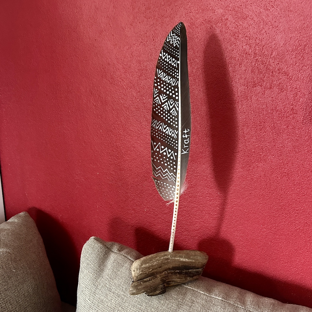 In Silber mit Zickzackmuster bemalte Feder vor roter Wand