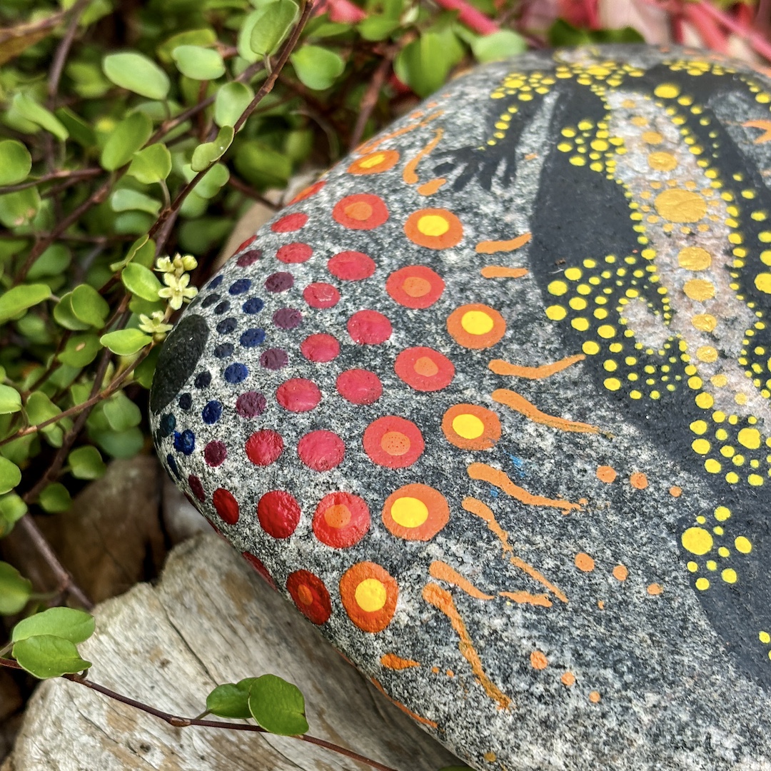 Stein mit einem Feuersalamder in Dot Painting Technik gestaltet auf Holz liegend in Nahaufnahme