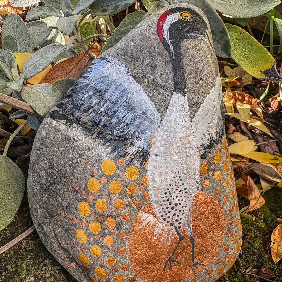 Stein im Garten stehend bemalt mit einem Kranich vor untergehender Sonne