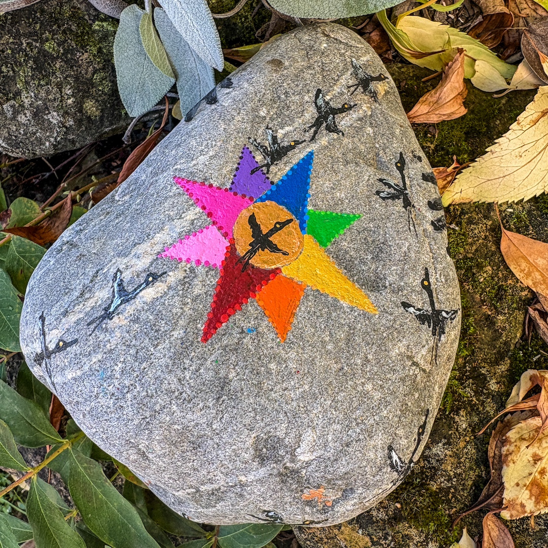 Stein im Garten stehend bemalt mit einem Kompass und fliegenden Kranichen 