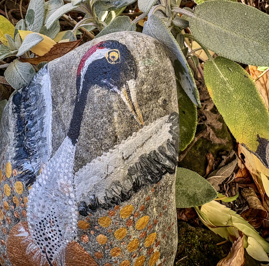 Stein im Garten stehend bemalt mit einem Kranich vor untergehender Sonne