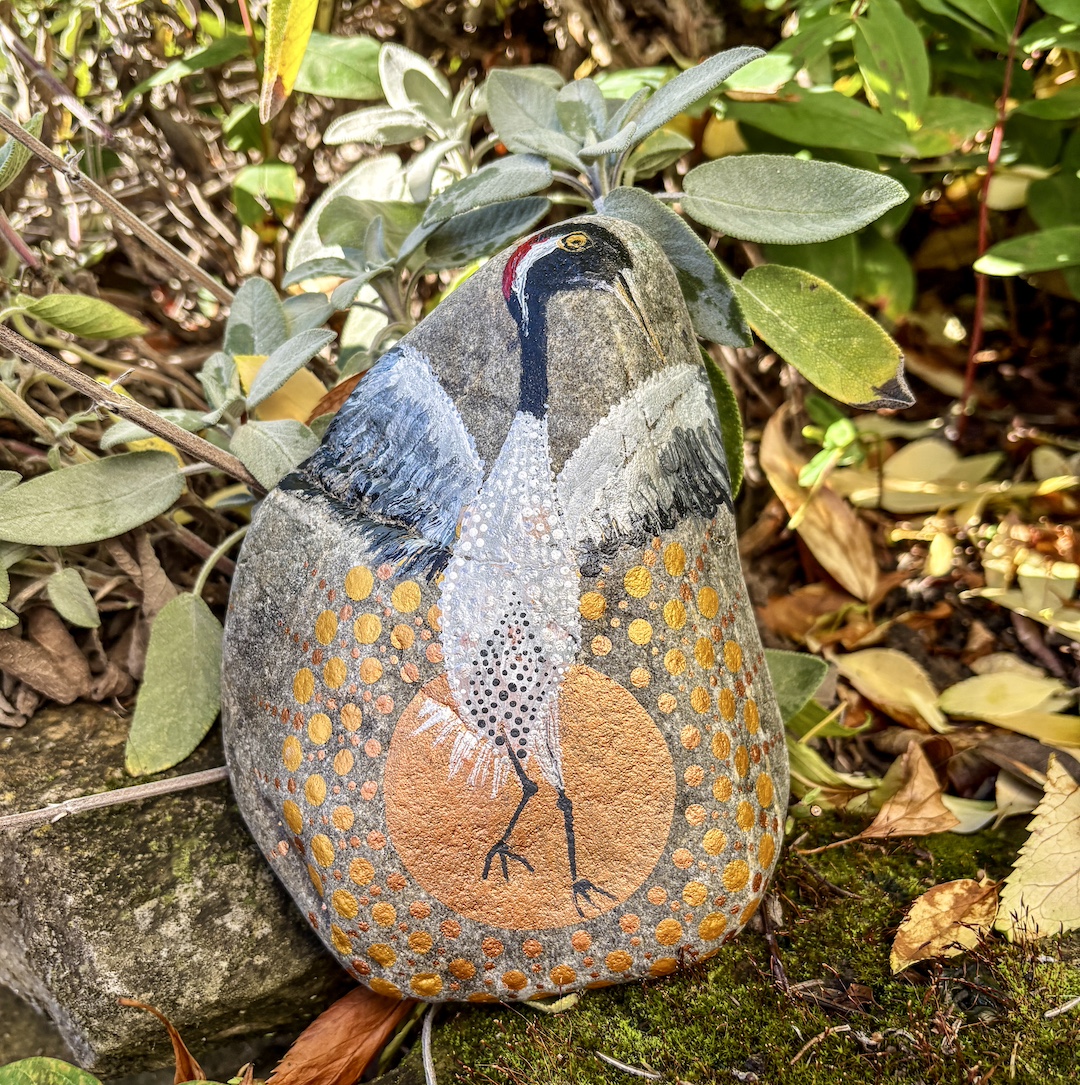 Stein im Garten stehend bemalt mit einem Kranich vor untergehender Sonne