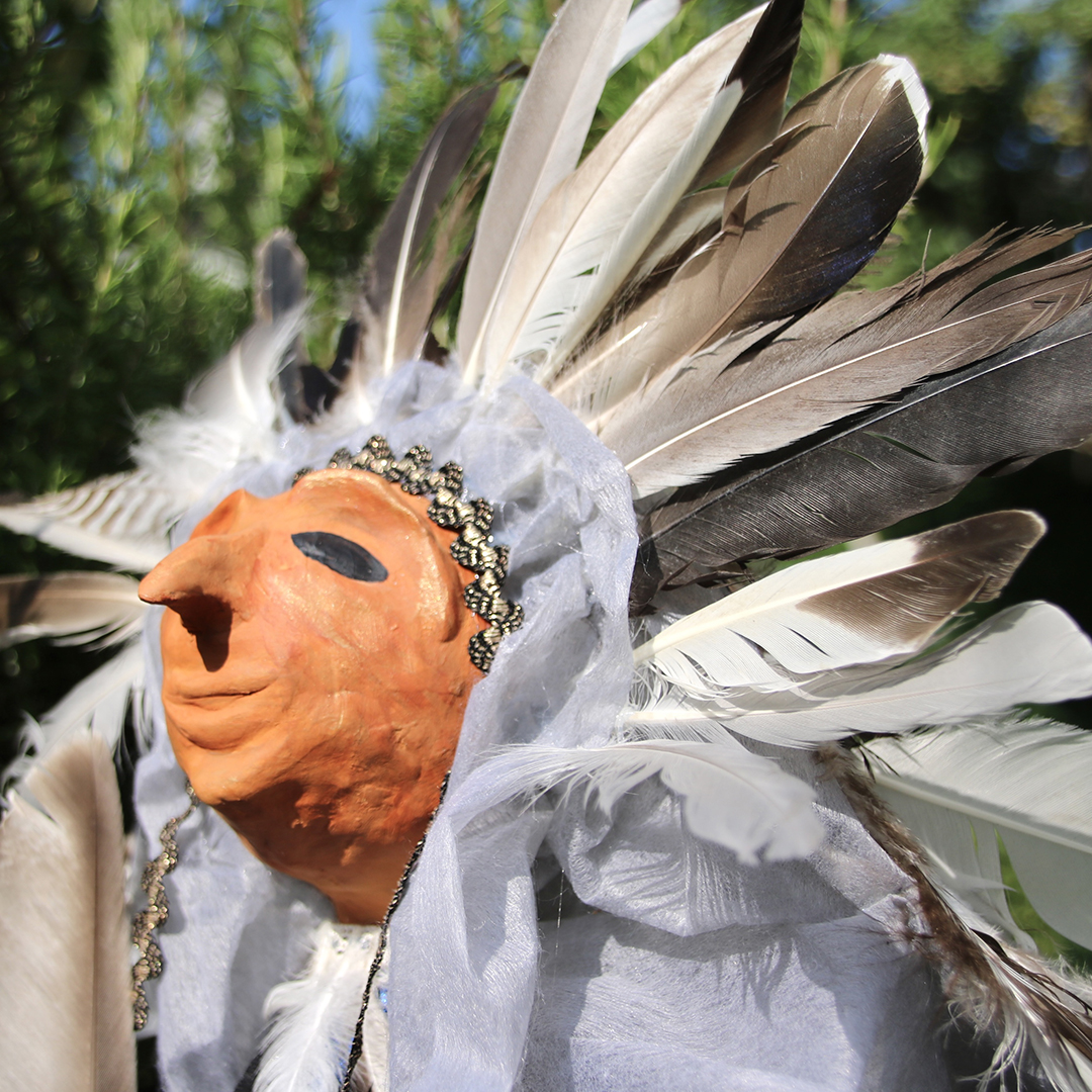 Kopf einer Stabfigur mit Federn geschmückt 