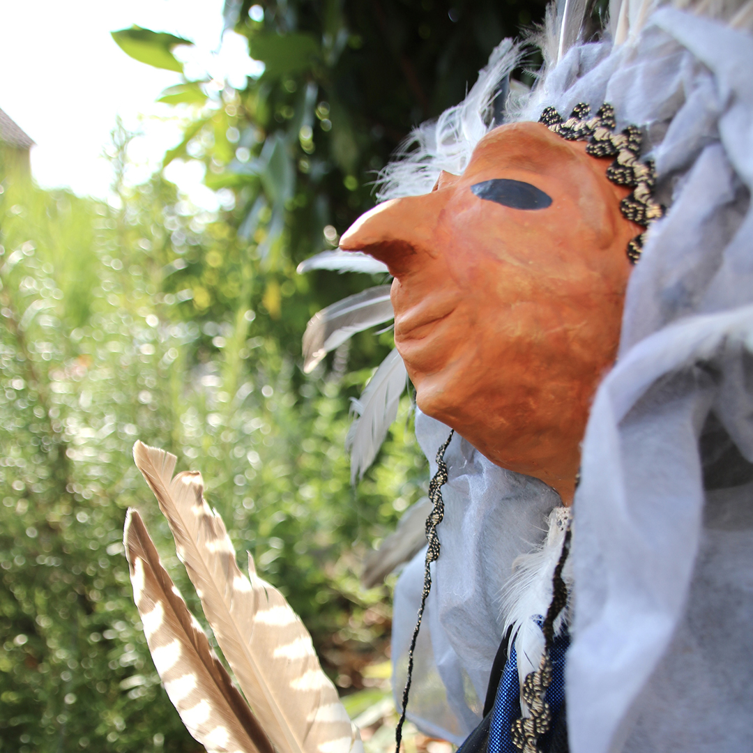 Stabfigur mit Stoffen und Federn geschmückt im Garten
